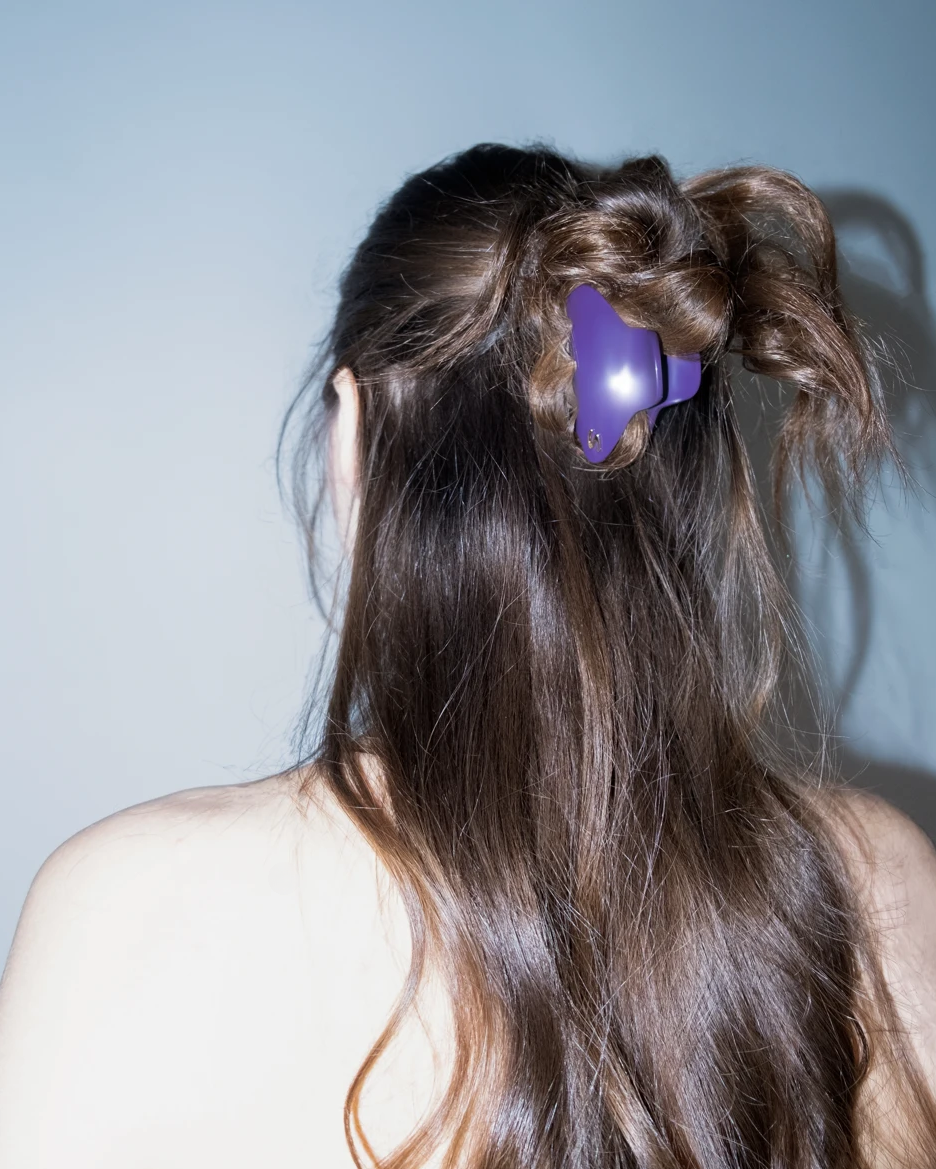Person with long hair styled in pigtails with a purple hair clip against a light blue background